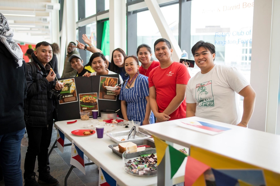 A group of students and community members stand behind a table with food on it from Philippines